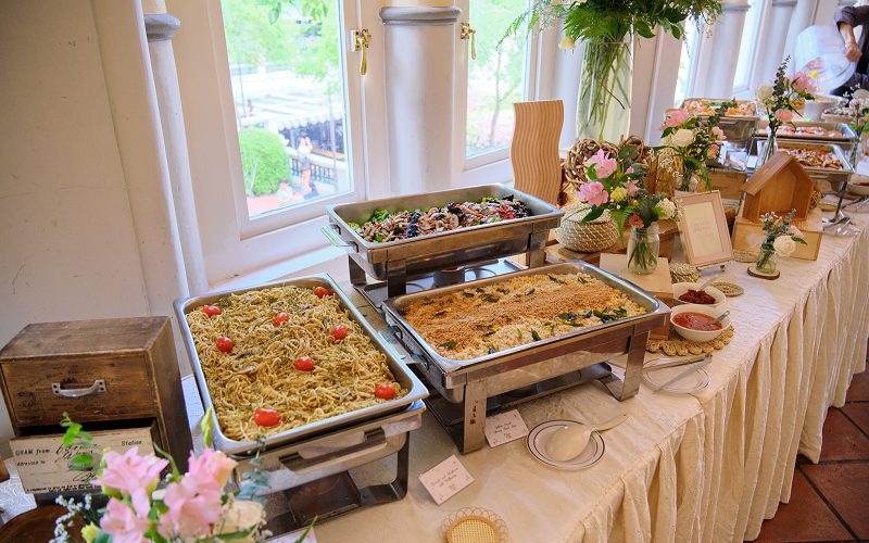 Long table buffet setup displaying catered hot food trays.
