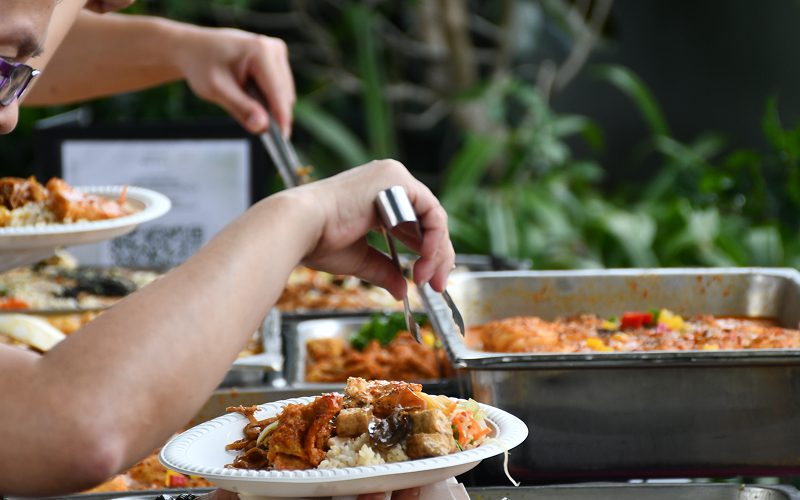 People using tongs to serve food at a buffet.