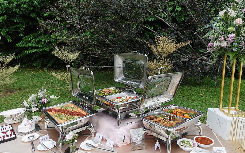 Outdoor catering buffet setup with chafing dishes in garden.